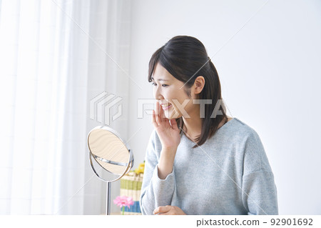 Woman doing skin care looking in the mirror at home Woman doing skin care looking in the mirror at home 92901692