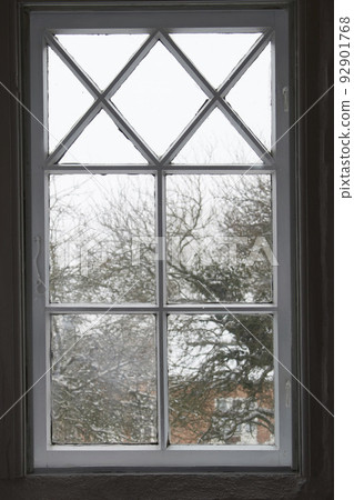 Closeup of a glass window from inside, looking out on cold weather in the morning. A wooden windowpane with bad insulation, shut and closed with a view of a winter scene with snow, frost and ice. 92901768