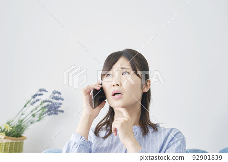 Woman calling on smartphone while thinking at home 92901839