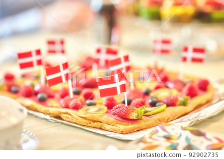 Danish fruit pastry for dessert to celebrate patriotism on Constitution Day in June. Annual holiday feast in Denmark with national flags in food. Fresh summer produce on a baked puff pastry 92902735