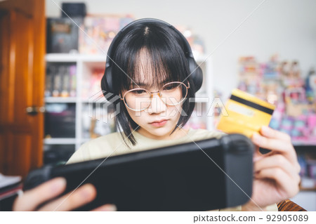 Nerd style young adult asian gamer using credit card for pay to win competition. Nerd style young adult asian gamer using credit card for pay to win competition. 92905089