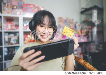 Nerd style young adult asian gamer using credit card for pay to win competition. Nerd style young adult asian gamer using credit card for pay to win competition. 92905090