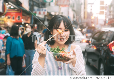 Young adult asian woman eating food of spicy grilled squid at southeast asia Chinatown market Young adult asian woman eating food of spicy grilled squid at southeast asia Chinatown market 92905212