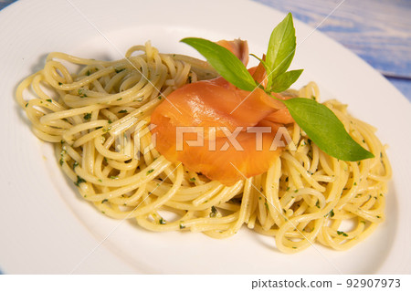 Pasta spaghetti with pesto sauce and fresh basil leaves in white plate, blue background Pasta spaghetti with pesto sauce and fresh basil leaves in white plate, blue background 92907973