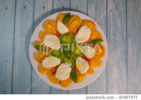 Green and Orange tomato and mozzarella salad with basil leaves and olive oil Green and Orange tomato and mozzarella salad with basil leaves and olive oil 92907975