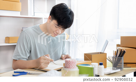 Sell online, Young man is writing down the customer's details and addresses on the notebook or box in order to prepare for shipping according to the information, Online shopping SME entrepreneur. 92908032