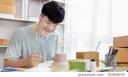 Sell online, Young man is writing down the customer's details and addresses on the notebook or box in order to prepare for shipping according to the information, Online shopping SME entrepreneur. Sell online, Young man is writing down the customer's details and addresses on the notebook or box in order to prepare for shipping according to the information, Online shopping SME entrepreneur. 92908034