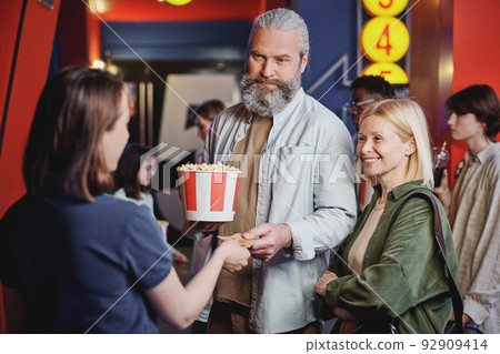 Modern mature couple passing their tickets for movie to young female cinema hall worker Modern mature couple passing their tickets for movie to young female cinema hall worker 92909414