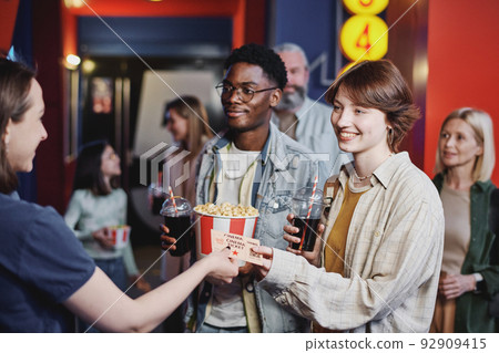 Joyful young Black man and Caucasian woman passing their tickets for movie to cinema hall worker 92909415