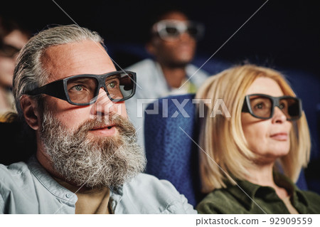 Selective focus shot of of handsome mature man with beard on face wearing 3D eyeglasses watching movie in cinema 92909559