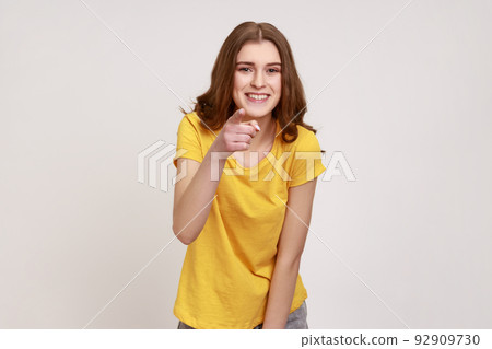 Hey you. Portrait of joyous young teenager girl in yellow T-shirt pointing finger at camera with happy face, choosing you, saying you are what we need. Indoor studio shot isolated on gray background. 92909730