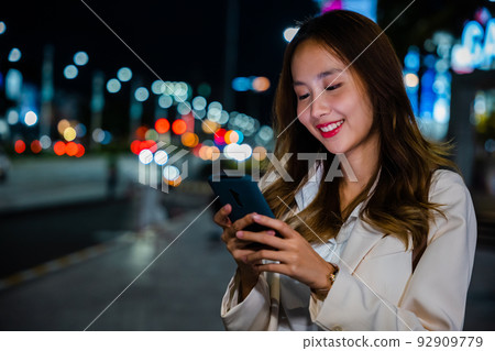 Business woman using mobile phone walking through night city street Business woman using mobile phone walking through night city street 92909779