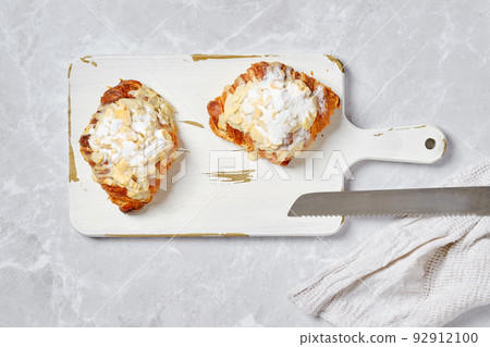 Overhead view of croissant with caramel and peanut shavings on white board on marble background Overhead view of croissant with caramel and peanut shavings on white board on marble background 92912100
