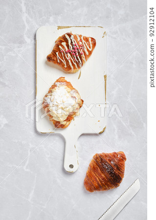 Overhead view of assortment of fresh croissants on serving board on marble background Overhead view of assortment of fresh croissants on serving board on marble background 92912104