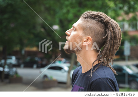 Side view of a caucasian man with dreadlocks and sidecut on a summer street 92912459