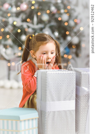 Emotional little girl with New Year gifts in white interior with christmas tree 92912462