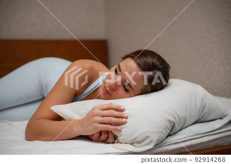 A young woman lies on a bed without a blanket. Bed linen is white. A young woman lies on a bed without a blanket. Bed linen is white. 92914268