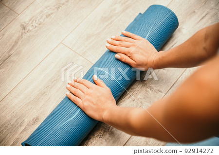 Woman hands rolled up yoga mat on gym floor in yoga fitness training room. Home workout woman close up hands rolling foam yoga gym mat. Woman barefoot home workout sportive healthy lifestyle concept Woman hands rolled up yoga mat on gym floor in yoga fitness training room. Home workout woman close up hands rolling foam yoga gym mat. Woman barefoot home workout sportive healthy lifestyle concept 92914272