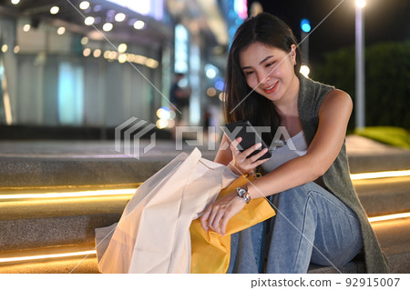 Beautiful young woman sitting on stairs in the night city and typing text message on her mobile phone Beautiful young woman sitting on stairs in the night city and typing text message on her mobile phone 92915007
