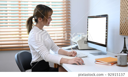 Side view young creative woman working online, searching information on computer in bright home office Side view young creative woman working online, searching information on computer in bright home office 92915137