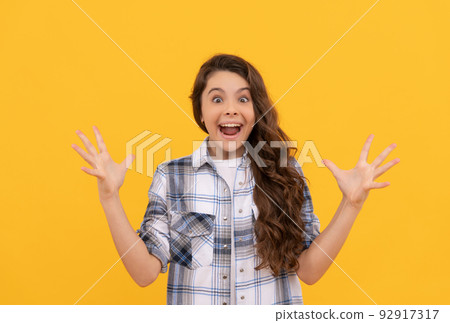amazed teen child in checkered shirt with long curly hair on yellow background 92917317