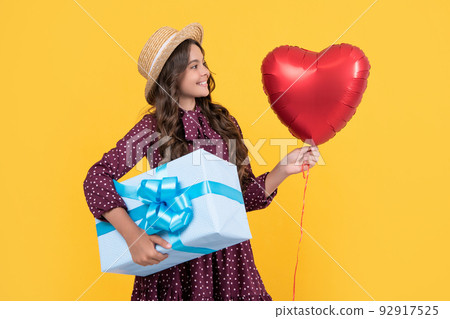 happy teen child with red heart balloon and present box on yellow background 92917525