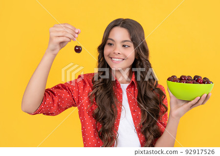happy teen girl hold cherry bowl on yellow background happy teen girl hold cherry bowl on yellow background 92917526