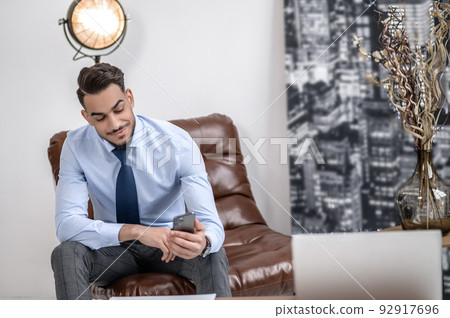 Happy man looking at smartphone sitting in office 92917696