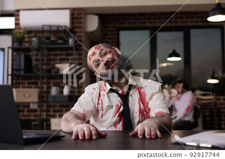 Portrait of walking dead corpse in office working on startup business with laptop, creepy evil monster sitting at desk. Brain eating horrific zombie with bloody wounds and dirty scars, eerie walker. Portrait of walking dead corpse in office working on startup business with laptop, creepy evil monster sitting at desk. Brain eating horrific zombie with bloody wounds and dirty scars, eerie walker. 92917744