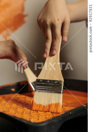 Small family using paintbrush and color to paint room walls, holding brush with bristles in liquid acrylic can. People painting apartment with paintwork tools, surface design renewal. Close up. Small family using paintbrush and color to paint room walls, holding brush with bristles in liquid acrylic can. People painting apartment with paintwork tools, surface design renewal. Close up. 92917831