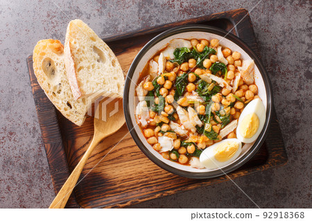 Chickpea stew with spinach and cod or potaje de vigilia close-up in a bowl on the wooden tray. Horizontal top view 92918368