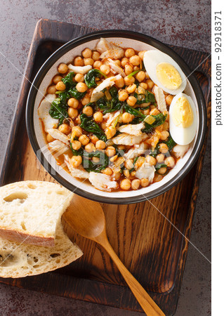 Potaje de Vigilia Spanish chickpea stew with cod and spinach close-up in a bowl on the wooden tray. Vertical top view Potaje de Vigilia Spanish chickpea stew with cod and spinach close-up in a bowl on the wooden tray. Vertical top view 92918371