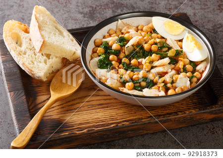 Chickpea stew with spinach and cod or potaje de vigilia close-up in a bowl on the wooden tray. Horizontal Chickpea stew with spinach and cod or potaje de vigilia close-up in a bowl on the wooden tray. Horizontal 92918373