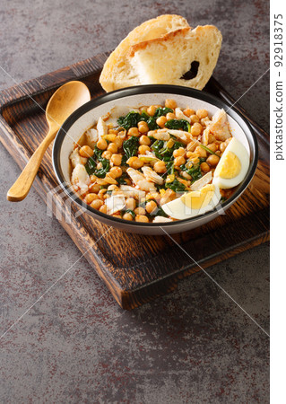Spanish Easter dish called potaje de vigilia using cod with chickpeas, smoked paprika and spinach close-up in a bowl on the wooden tray. Vertical Spanish Easter dish called potaje de vigilia using cod with chickpeas, smoked paprika and spinach close-up in a bowl on the wooden tray. Vertical 92918375