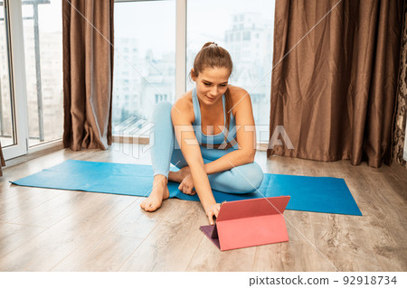 Young athletic attractive woman practicing yoga doing exercises. Works out at home or in a yoga studio, sportswear, blue pants and a full-length top indoors. Healthy lifestyle concept Young athletic attractive woman practicing yoga doing exercises. Works out at home or in a yoga studio, sportswear, blue pants and a full-length top indoors. Healthy lifestyle concept 92918734
