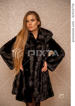 Young beautiful glamorous woman in a black luxurious fur coat posing against the background of a golden wall. fashion portrait Young beautiful glamorous woman in a black luxurious fur coat posing against the background of a golden wall. fashion portrait 92918736