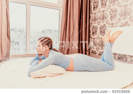 Side view portrait of relaxed woman with long hair lying on carpet at home. She is wearing a blue tracksuit. 92918808