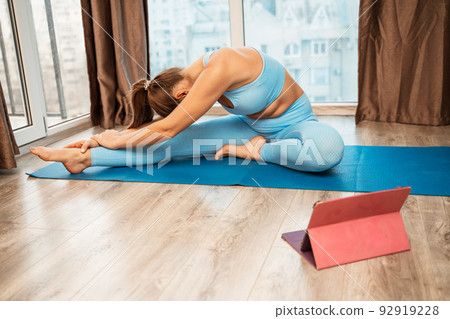 Young athletic attractive woman practicing yoga doing exercises. Works out at home or in a yoga studio, sportswear, blue pants and a full-length top indoors. Healthy lifestyle concept 92919228