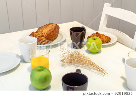 Fresh tasty breakfast served on a white table with croissants, apples and orange juice. 92919825