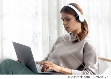 Happy young woman wearing headphones listening music while using laptop computer and singing. 92920176
