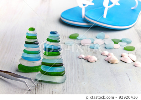 Pyramid of balanced sea-polished multicolored glass stones on a white wooden deck chair on the beach 92920410