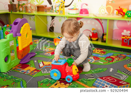A small two-year-old girl plays with toys in the playroom. Development Centre, Kindergarten A child plays with a steam train on the carpet. Lots of different toys in the background 92920494