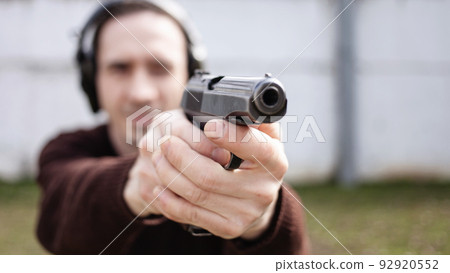 A young man is aiming for a gun. A man wearing protective headphones. outdoor tyre shooting range. hobby. firearm against the white wall 92920552