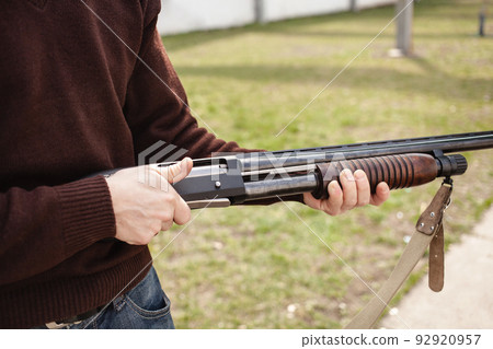 A young man charges a pump-action shotgun with a Ammo. 12 caliber. Tyre outdoor. A man in headphones and goggles is preparing to shoot. Firearms for sports shooting, hobby. 92920957
