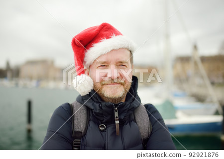 Man wearing a santa hat walks in port of Lausanne on shores of Geneva lake on Christmas eve. Winter holidays in Switzerland, Europe Man wearing a santa hat walks in port of Lausanne on shores of Geneva lake on Christmas eve. Winter holidays in Switzerland, Europe 92921876