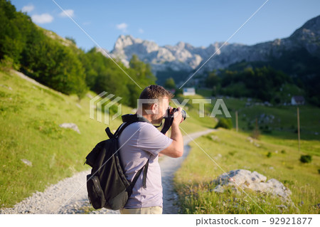 Mature man tourist with backpack and camera is hiking on mountain valley. Photographer taking a picture during travel. Mature man tourist with backpack and camera is hiking on mountain valley. Photographer taking a picture during travel. 92921877