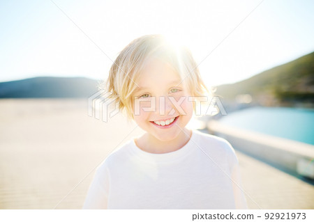 Portrait of cheerful smiling schoolboy child by sea during summer holidays on sunny day. Concept of freedom, happy childhood and limitless possibilities. 92921973