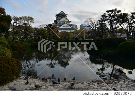 Osaka Prefecture, Japan, Osaka Castle in spring, cherry blossoms in full bloom and a splendid castle tower, a flock of pigeons resting around a pond 92923073