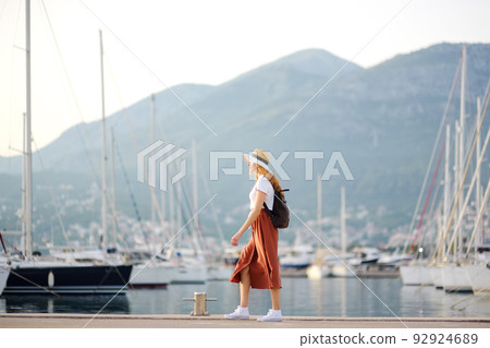 Charming young tourist woman travel by Mediterranean coast. Attractive red-haired girl on the background of sea and yachts. Yacht rental. Charming young tourist woman travel by Mediterranean coast. Attractive red-haired girl on the background of sea and yachts. Yacht rental. 92924689