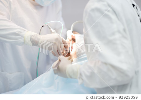 Surgeon and nurse during a dental operation. Anesthetized patient in the operating room. Installation of dental implants in the clinic. 92925059